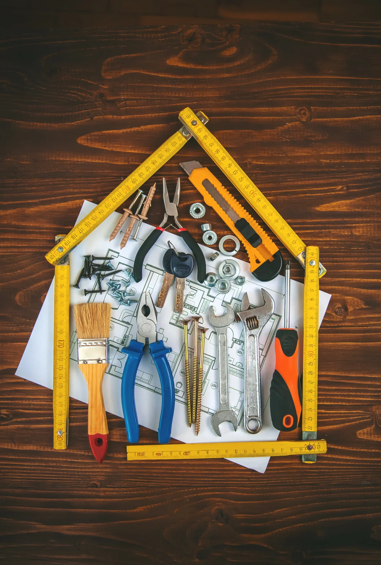 A construction ruler shaped like a house with construction tools and a floor plan sketch inside of it.