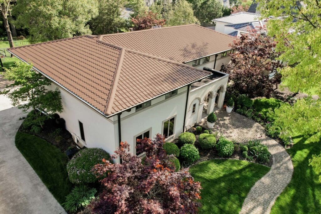 A modern two-story house with a tiled roof surrounded by lush greenery.