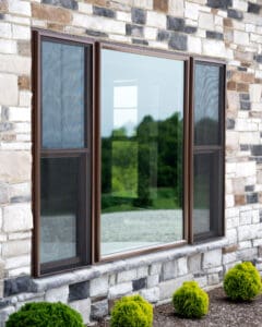 Modern stone wall with a large triple-pane glass window reflecting greenery.