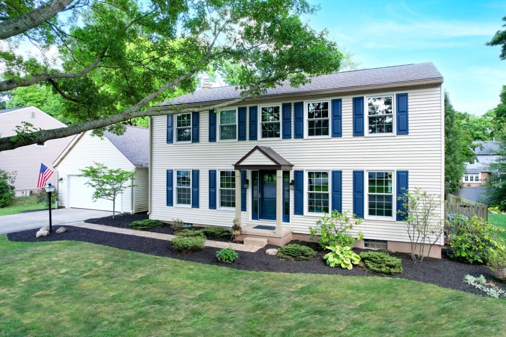 A charming two-story white house with blue shutters and a neatly landscaped yard.