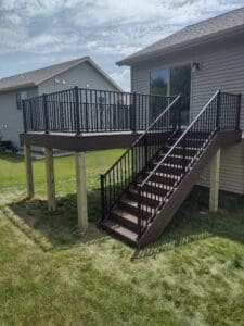 Elevated wooden deck with black metal railing and stairs attached to a house.