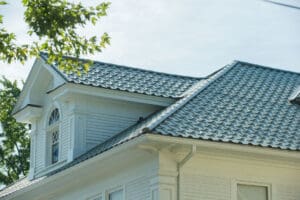 A close-up of a house roof with blue tiles and a small window under a tree.