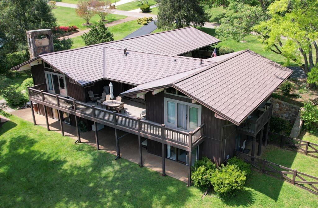 A large wooden house with a spacious balcony surrounded by greenery.