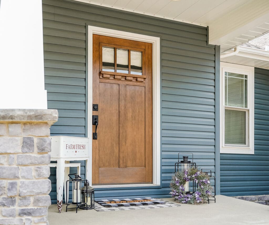 A wooden front door with glass panels on a blue house exterior.