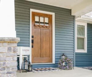 A wooden front door with glass panels on a blue house exterior.