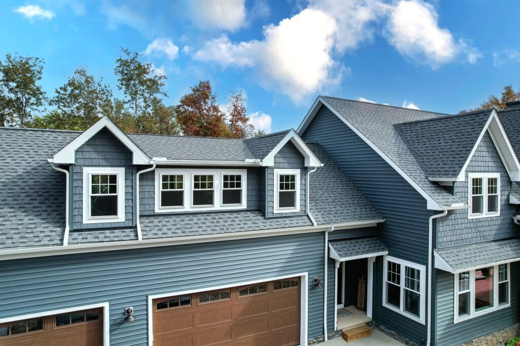 Blue two-story house with garage and dormer windows under a partly cloudy sky.