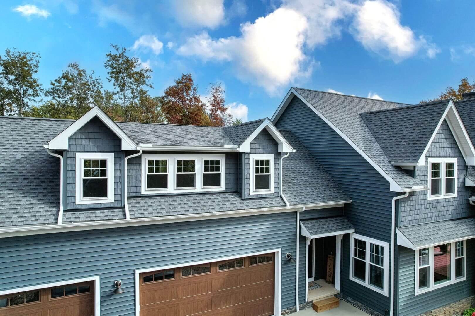 Blue two-story house with garage and dormer windows under a partly cloudy sky.