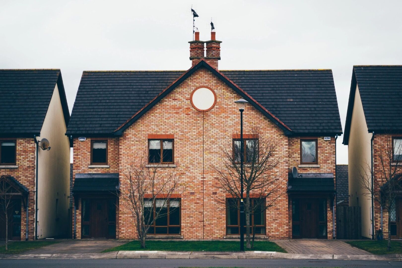 Symmetrical brick house with a circular window in the center, flanked by two smaller houses.