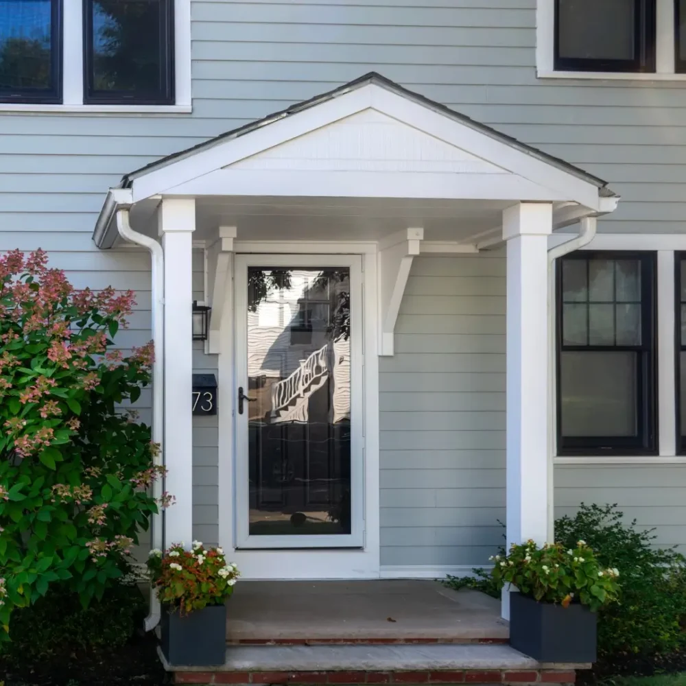 Front entry of a family home with gabled portico and storm door.