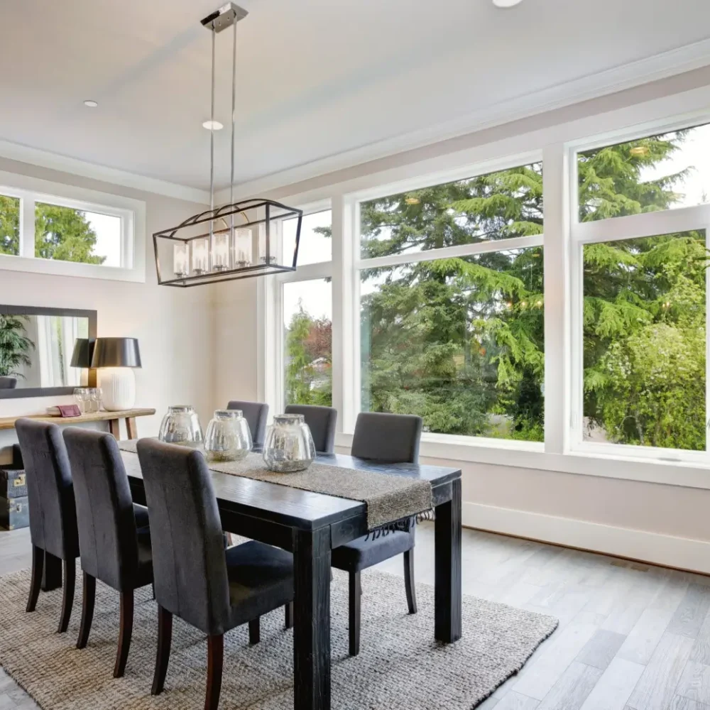 Luxurious modern dining room boasts a black dining table and large windows looking out to the top of some trees.