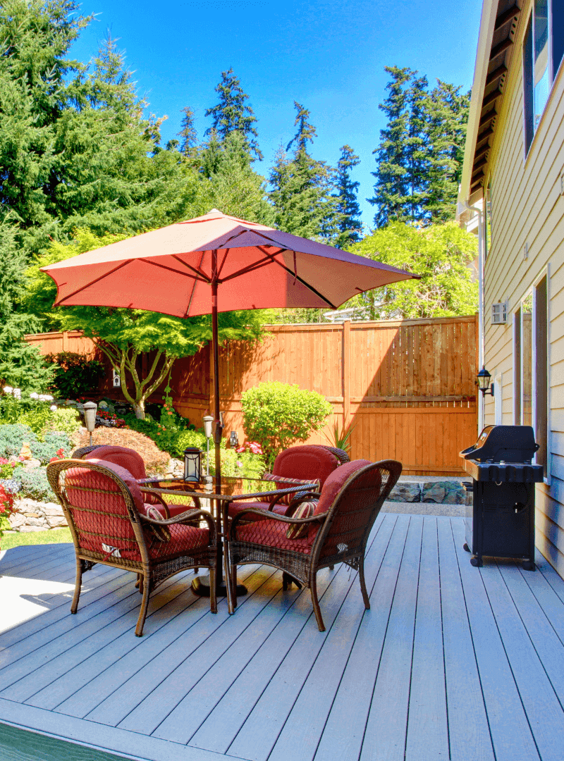 A patio with an umbrella and chairs on the deck.