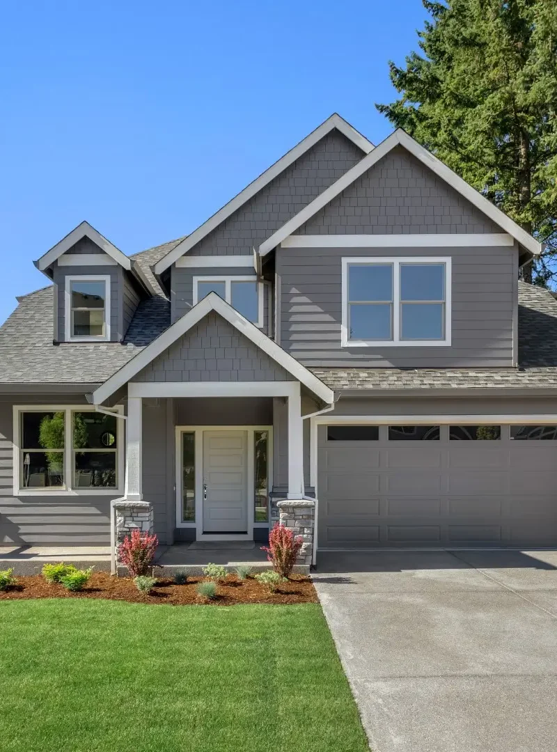 Suburban home exterior on bright sunny day with large yard and covered porch.