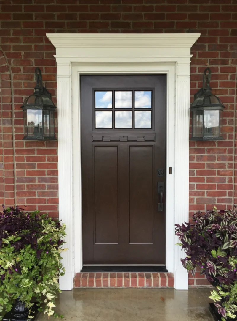 An elegant mahogany front door placed on a brick wall with two street lamps on both sides of it.