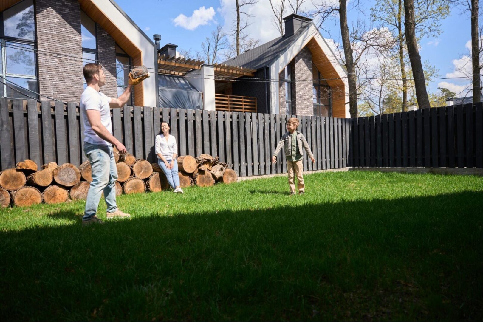 Family playing catch on a lawn next to a fence. 