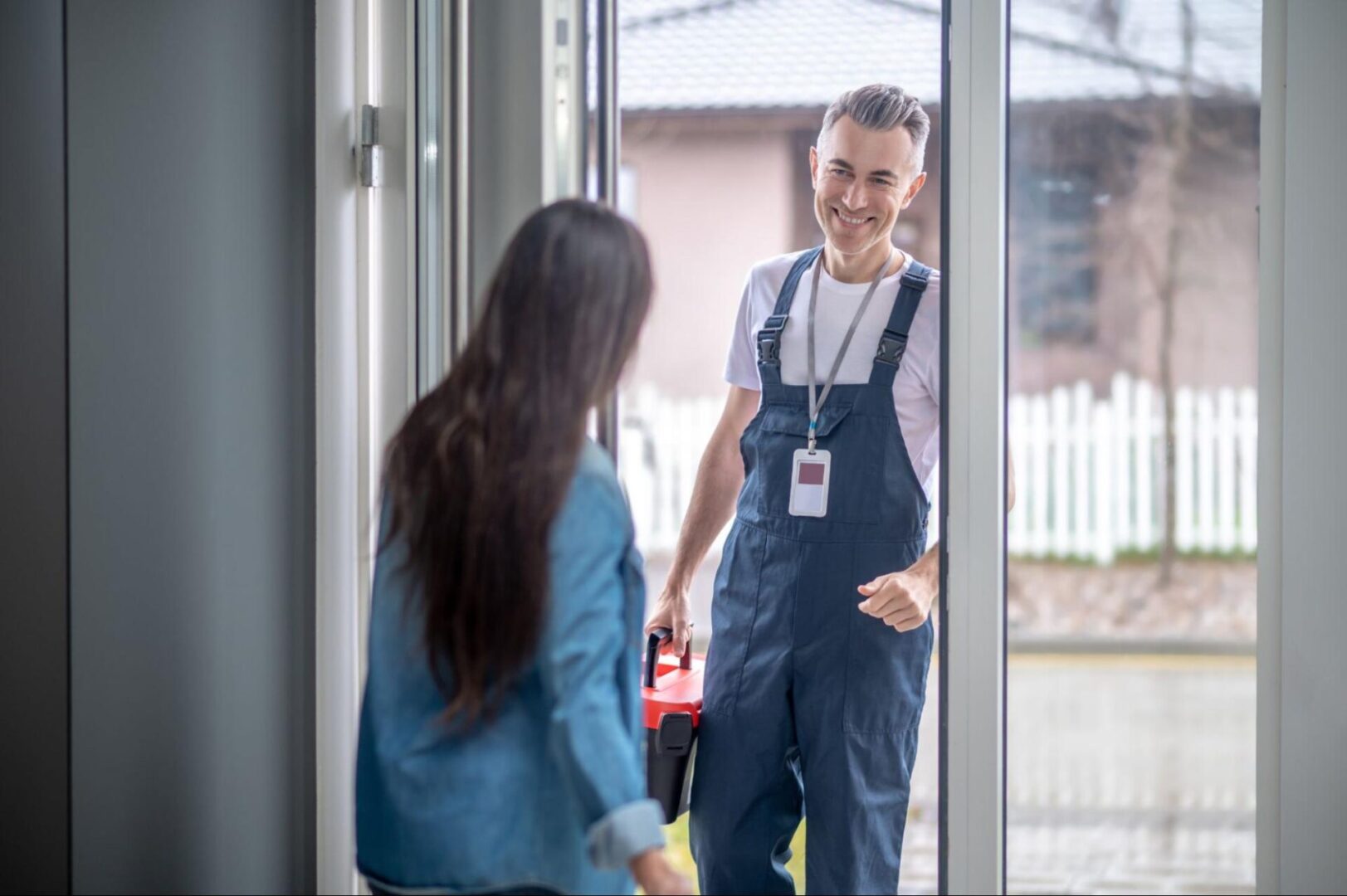 A woman welcomes a repairman holding a toolbox. 