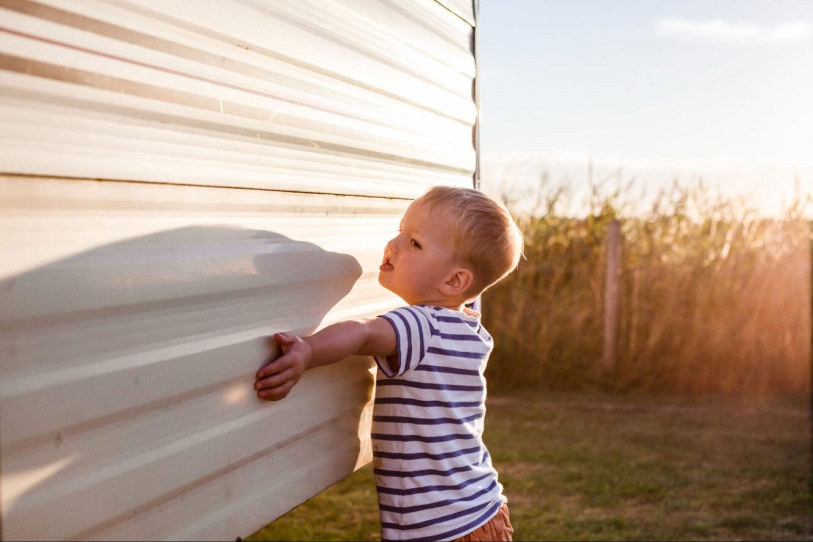 Young boy touching the side of a home with siding. 