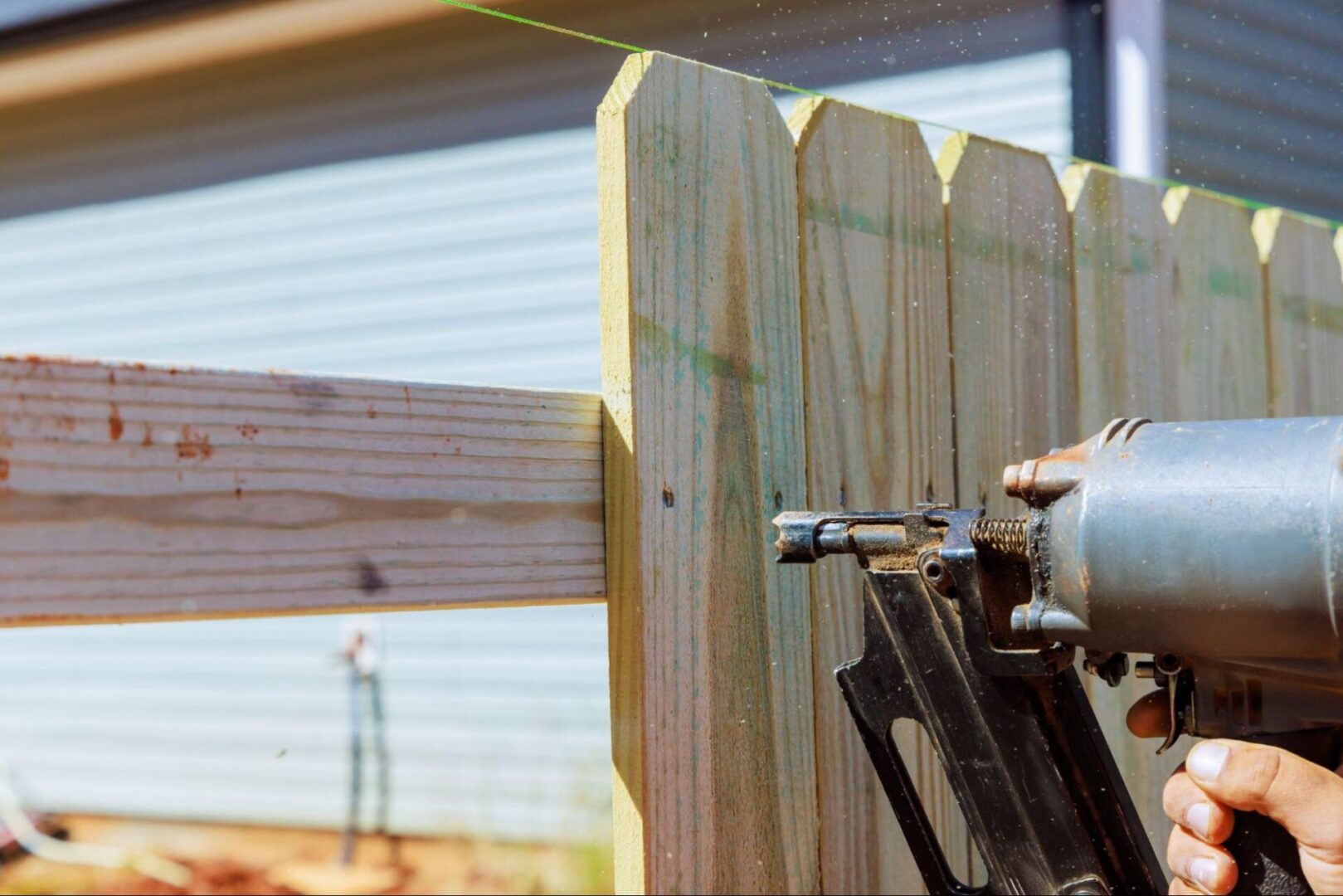 A repairman uses an air pneumatic gun to secure the wooden fence. 