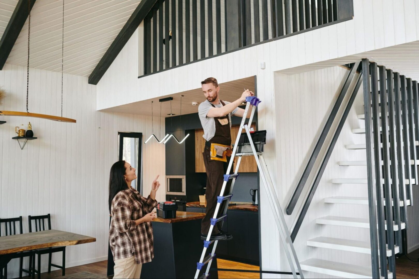 Woman next to a remodeler on a ladder working on her home. 