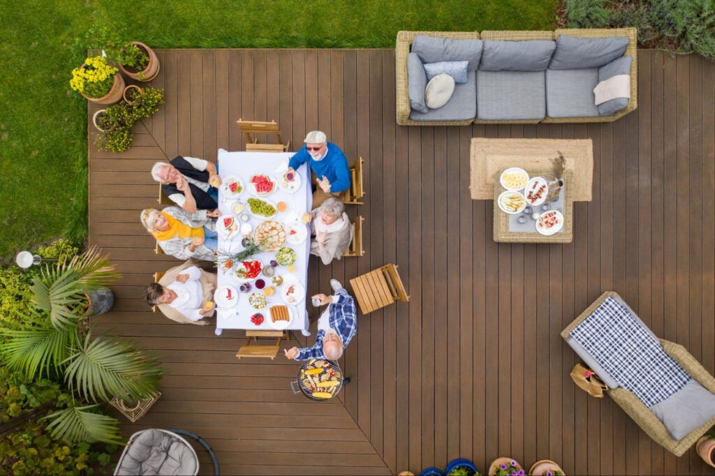 An aerial view shows a group of elderly friends enjoying dinner on a cozy patio made of high-quality decking materials.