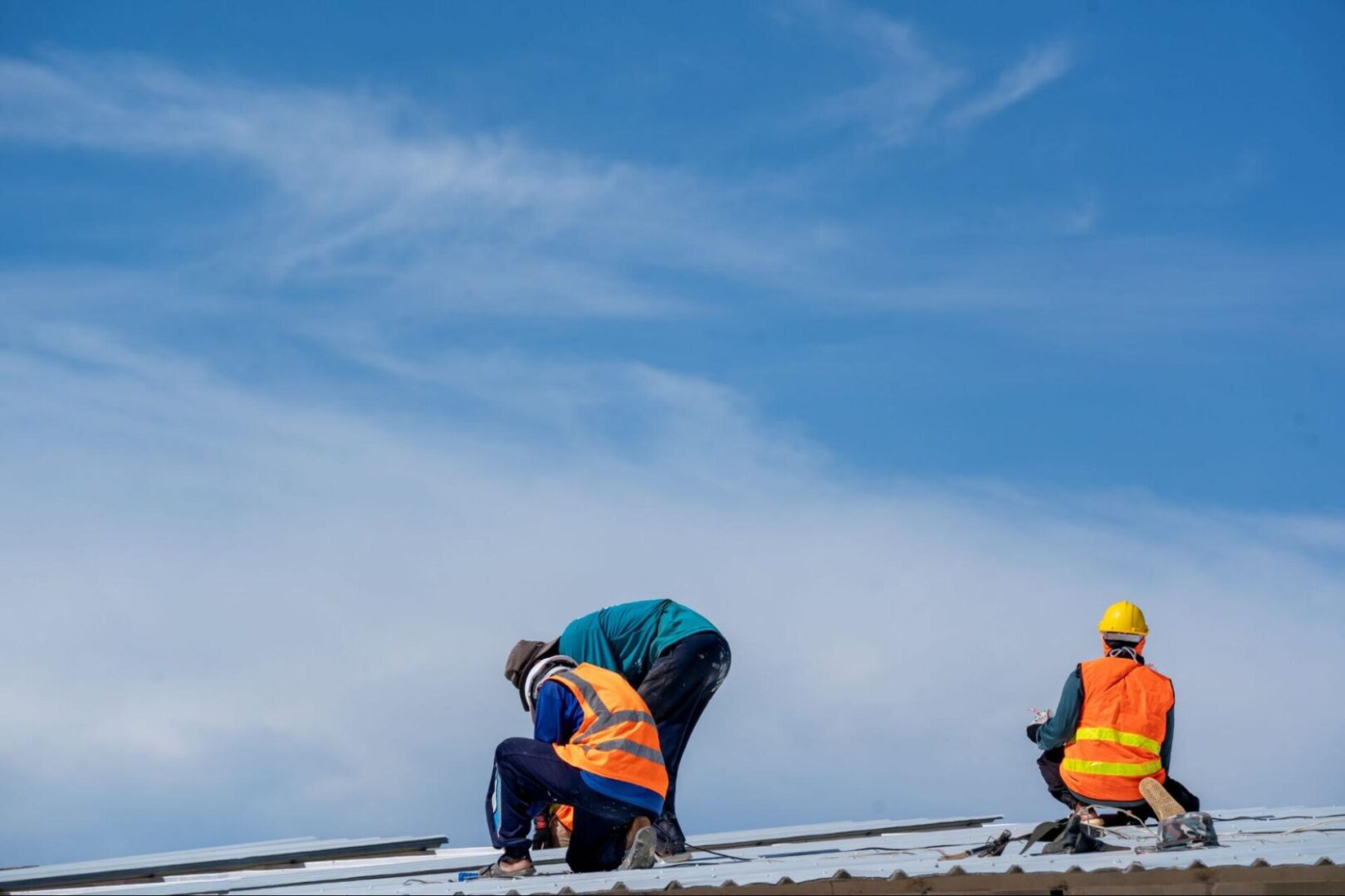 Construction workers in vests and hard hats on a roof with an open sky in the background. 