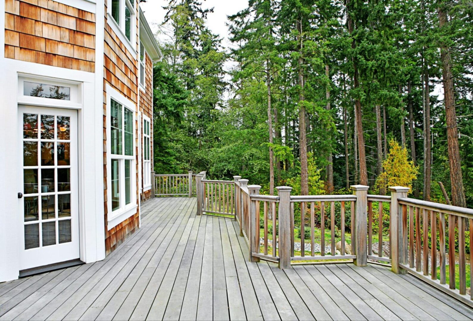 Wooden deck and railing next to a forest at the back of a house. 