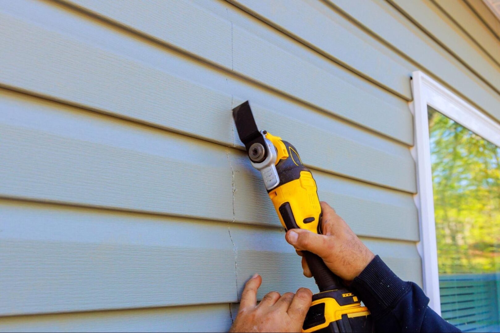 A close-up of a multi-tool removing the damaged vinyl siding from a house exterior.