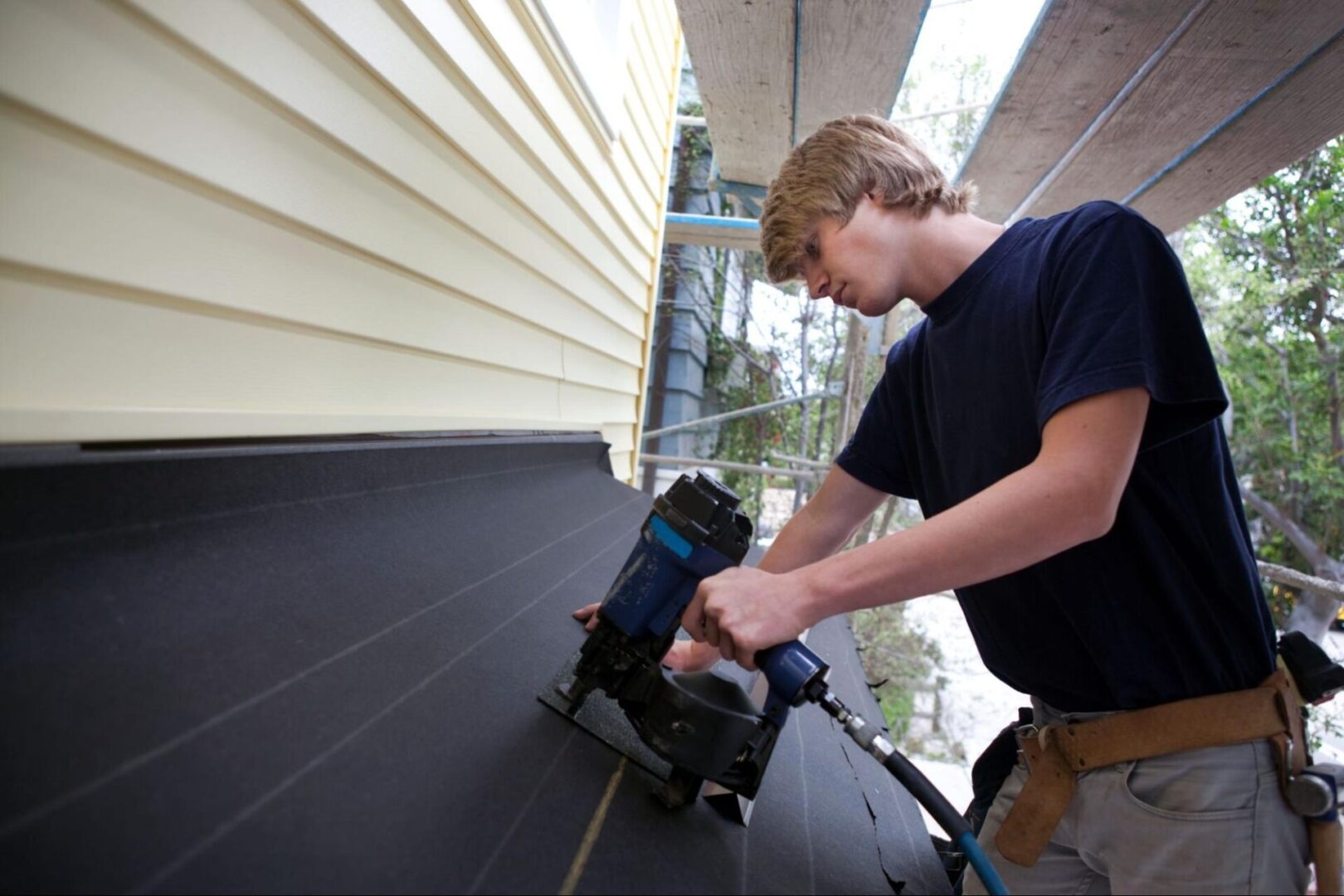 A young man uses a nail gun to repair siding on a home, showcasing the precision and tools used in professional siding repair work.