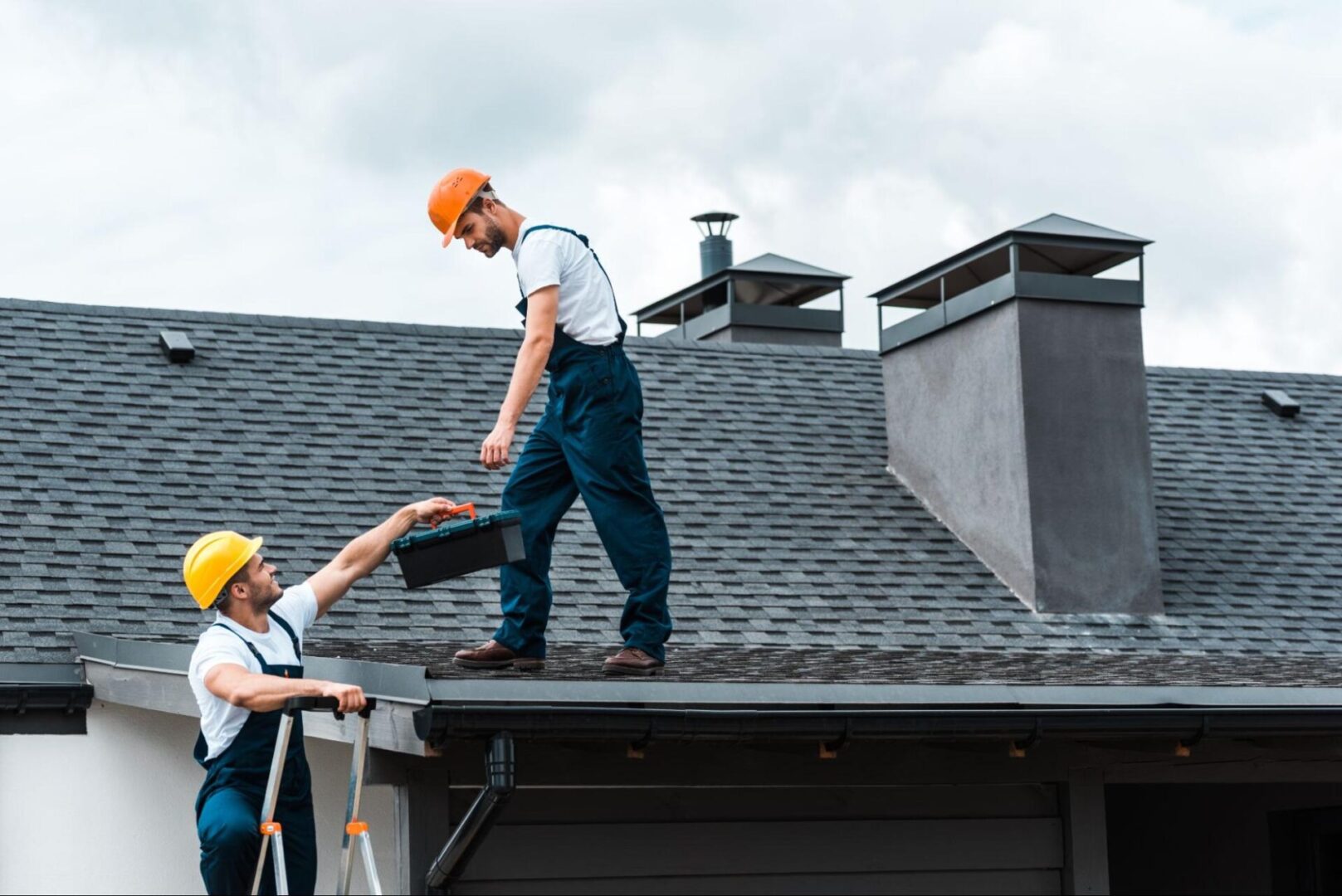 A carpenter wearing a yellow hat gives the tools box to his colleague.