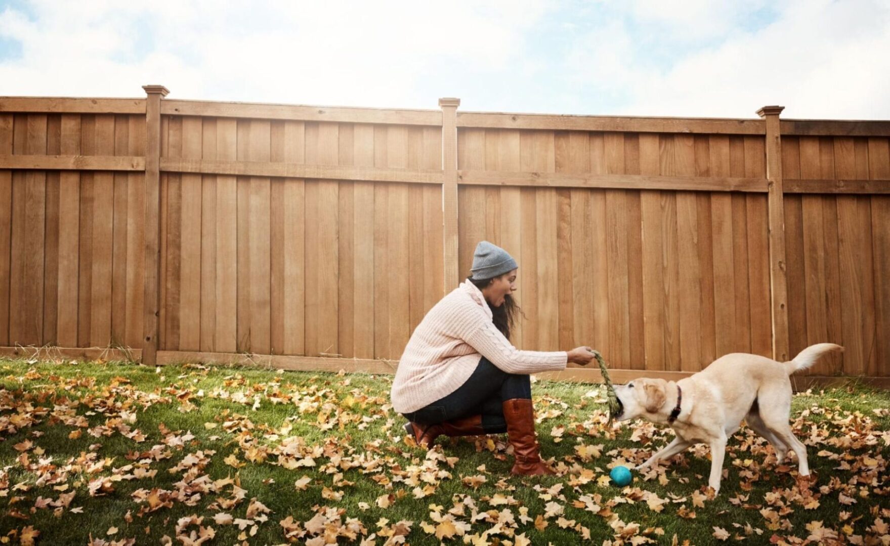 Woman playing with her dog in the backyard next to a tall wooden fence. 