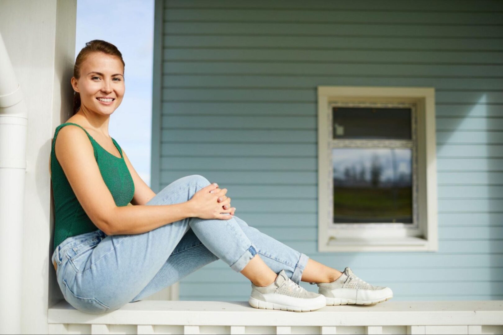 Woman sitting on a ledge next to siding on her home. 