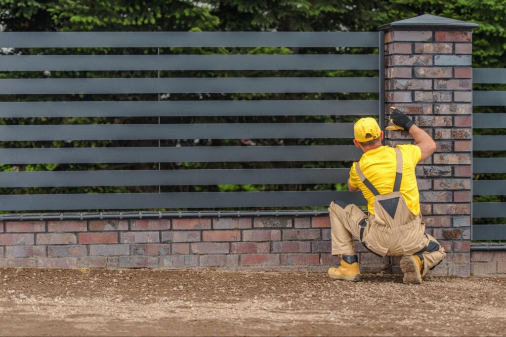 Fencing contractor working on a metal and brick fence.