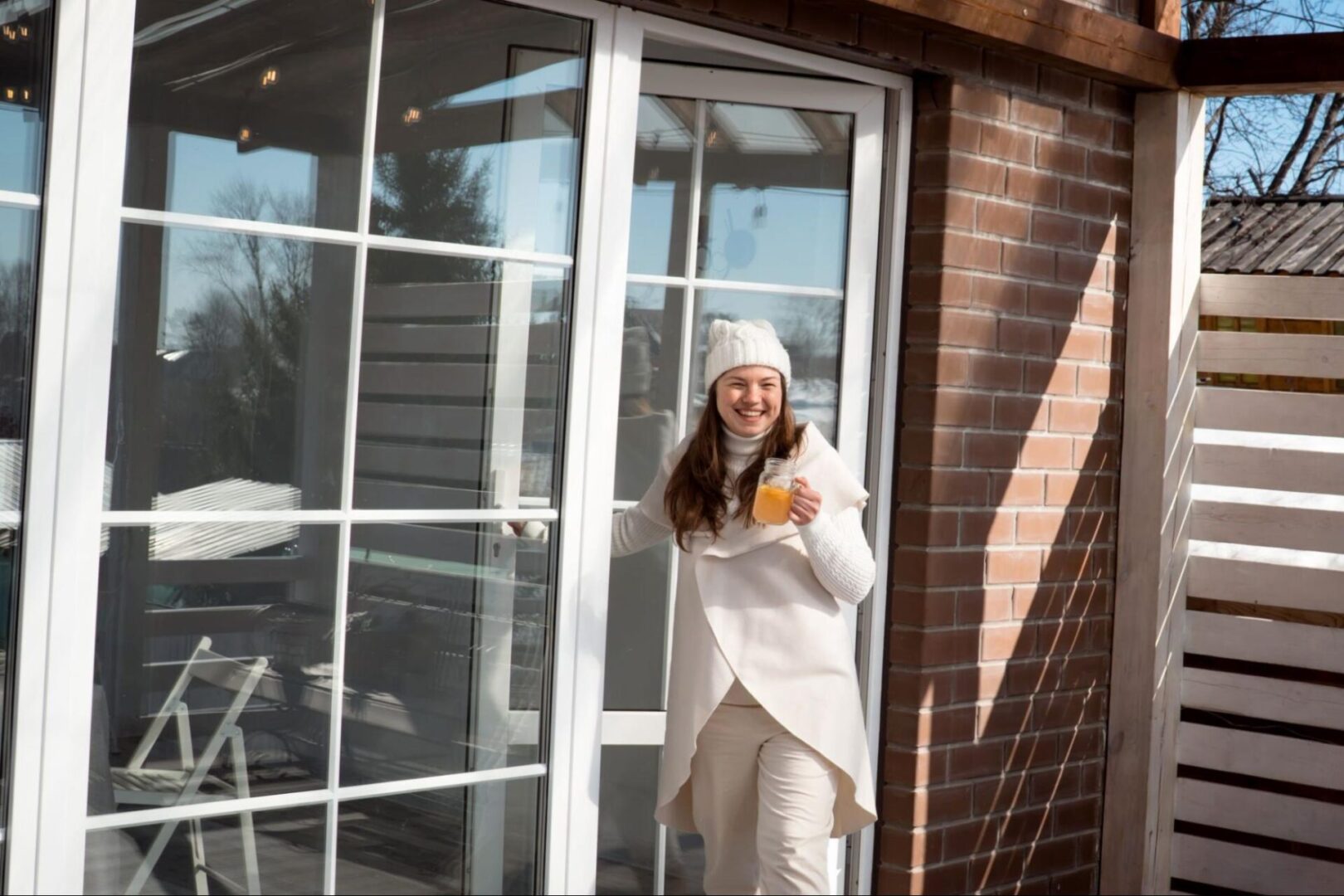 A woman holds a drink while stepping through a storm door with a sleek white frame and large glass panels.