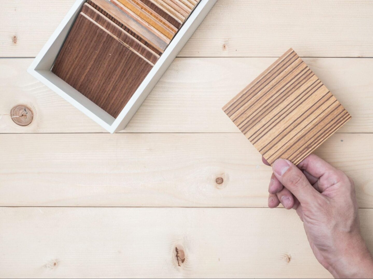 A hand holding a deck material sample from a box of swatches. 