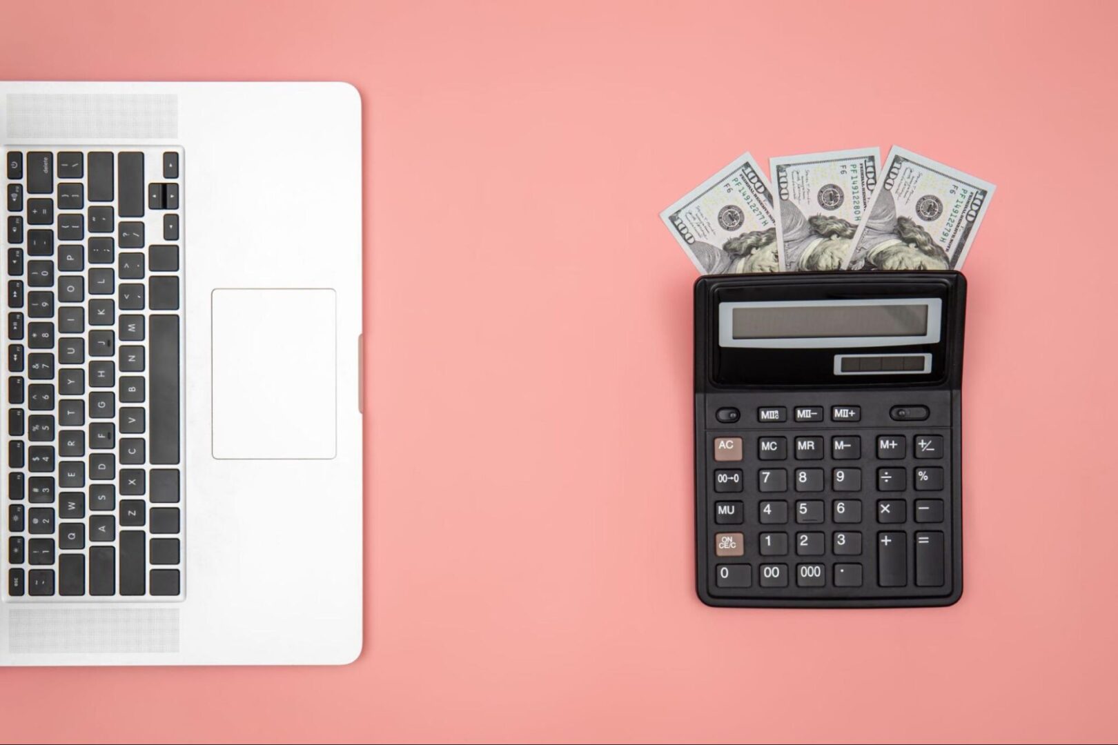 Calculator next to money and a laptop. 