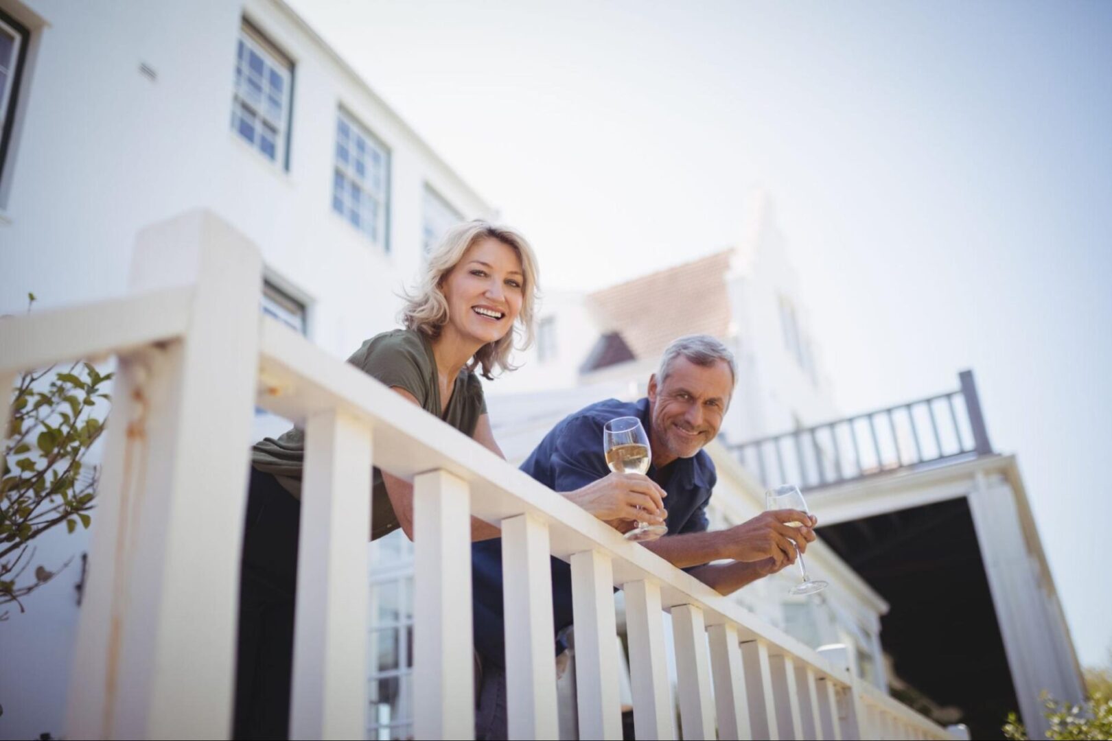 Couple leaning on deck railing and holding glasses of wine. 